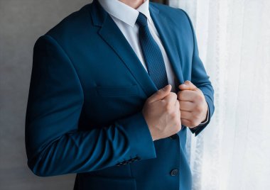 Beyaz gömlekli ve kravatlı bir işadamı pencerede duran mavi takımı ayarlar..