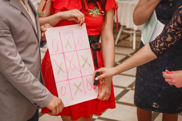 A group of people play the game of crosses and zeros on a large white sheet of paper.