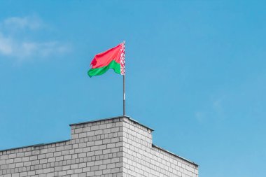 Mavi gökyüzüne karşı tuğla bir binanın kenarında Beyaz Rusya bayrağı.