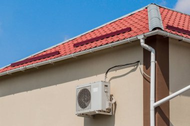 Modern bir binanın ya da çatının yanındaki evin duvarında mavi gökyüzüne karşı klima duruyor..