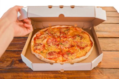 Adamın eli, tahta bir masanın arka planına karşı bir kutu pizza açıyor. Lezzetli fast food.