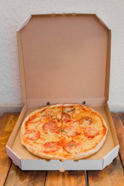 Tahta bir masa üzerinde peynirli ve salamlı yeni yapılmış pizza için karton paketi aç.