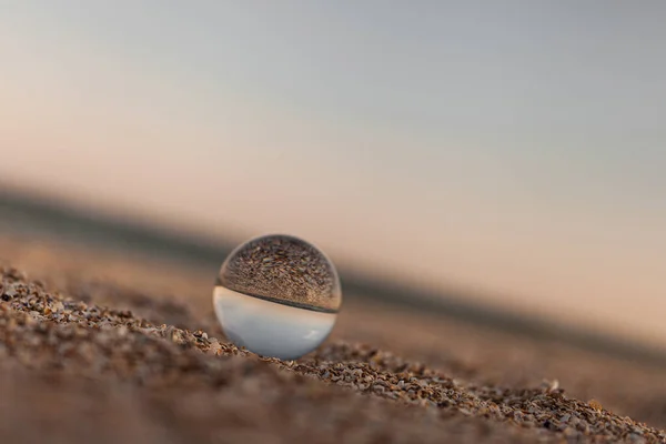 Glass optical ball on the sandy azure coast of the sea — Stock Photo, Image