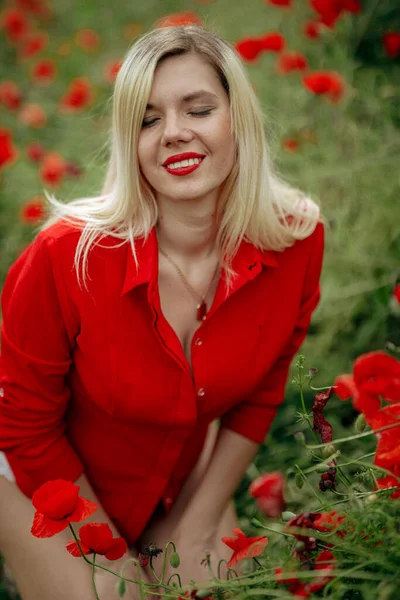 Hermosa chica en un campo con amapolas rojas en una camisa roja —  Fotos de Stock