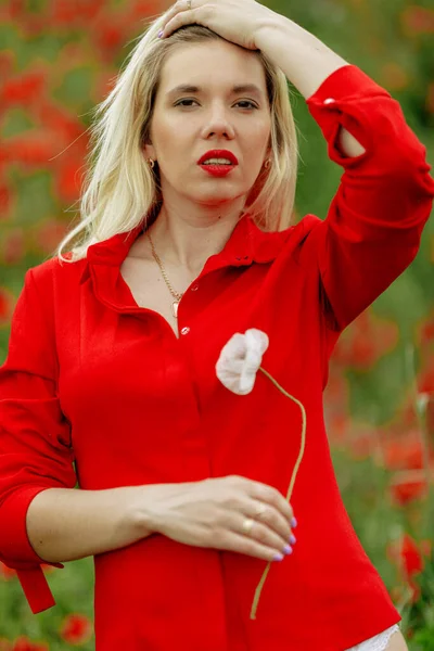 Hermosa chica en un campo con amapolas rojas en una camisa roja —  Fotos de Stock