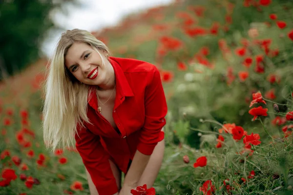 Hermosa chica en un campo con amapolas rojas en una camisa roja —  Fotos de Stock