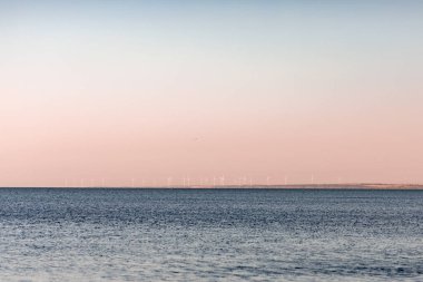 Okyanus kenarında günbatımı güneşi, berrak su ve kumlu gök mavisi plajı.