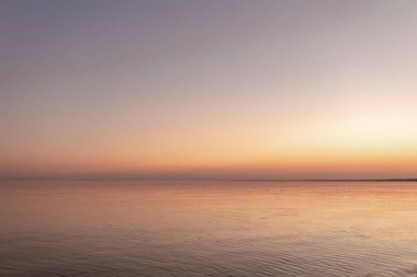Okyanus kenarında günbatımı güneşi, berrak su ve kumlu gök mavisi plajı.