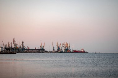 Okyanus kenarında günbatımı güneşi, berrak su ve kumlu gök mavisi plajı.