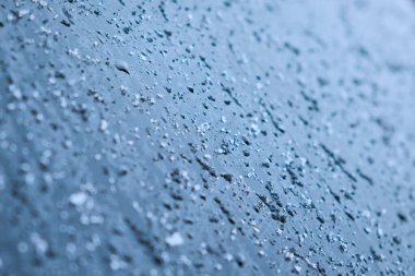 Cam yüzeyde eriyen kar ve su damlaları. Soyut mavi ton arkaplanı. Seçici odak.