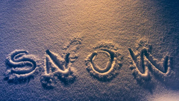 Text SNOW na sněhovém povrchu v noci zesvětlit v teplém oranžovém světle. — Stock fotografie