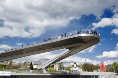 Moskova nehrinin yukarısında, Zaryadye parkında bir sürü insanla birlikte yüzen köprü. Kızıl Meydan yakınlarında, bulutlu mavi gökyüzüne karşı, gündüz vakti şehir manzaralı. .