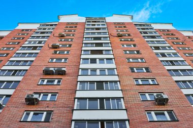 Mavi gökyüzüne karşı pencereleri ve balkonları olan yüksek modern tuğlalı bina duvarı.