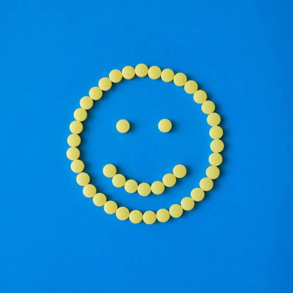 Smiling face from yellow round pills on blue background. Tablets, vitamins, medicine concept. — Stock Photo, Image