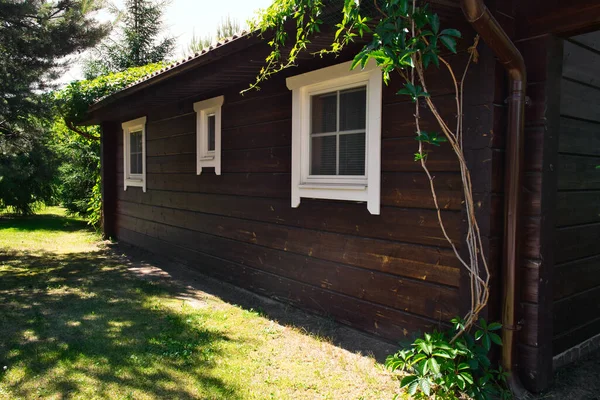 Casa de campo de madeira escura simples no dia de verão ensolarado. A parede da casa de hóspedes com três janelas. — Fotografia de Stock