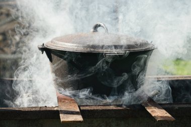 Şenlik ateşinin üzerindeki kazan dumanla kaplanmış. Metal tencerede dışarıda yemek pişirmek..