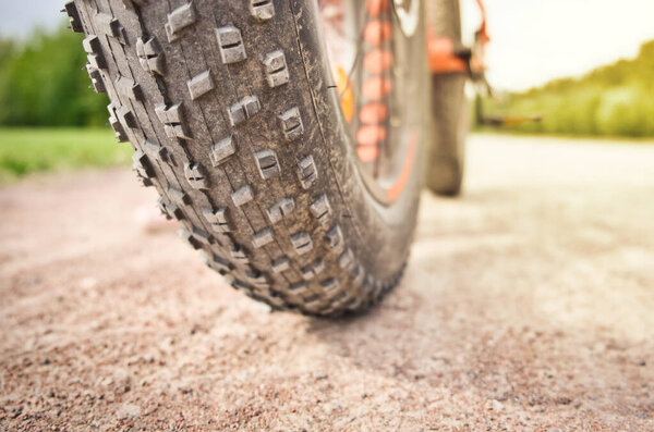 Close-up of fat mountain bike tire on dirty road. Fat bike wheel. Summer outdoor activity concept.