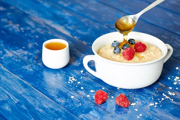 Breakfast with porridge, berries and honey on wooden table