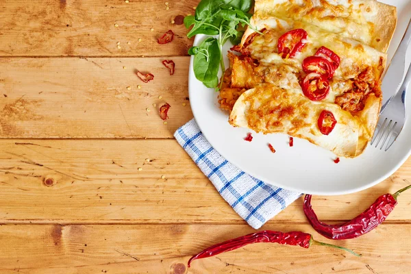 Enchiladas dish with red chili peppers on wooden table — Stock Image Enchiladas dish with red chili peppers on wooden table Stock Picture