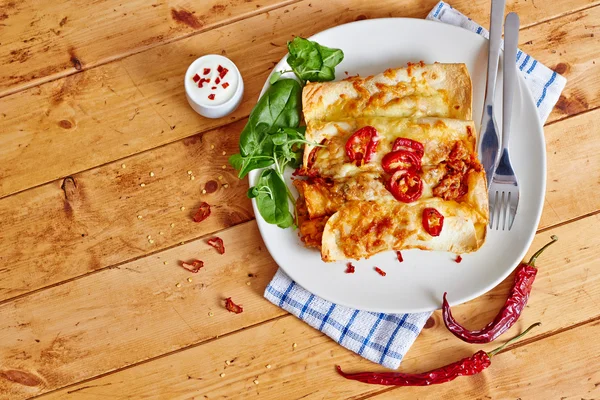Enchiladas dish with red chili peppers on wooden table — Stock Image Enchiladas dish with red chili peppers on wooden table Stock Picture