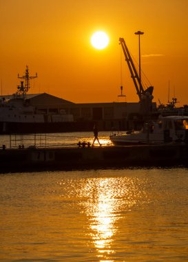 Kız gün batımında limanda yürüyor.