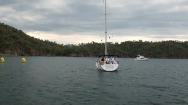 Sahildeki deniz ve dağların arka planında beyaz bir yat var..