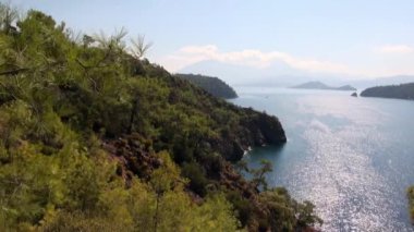 Güneş ışınları, deniz suyunun yüzeyinde, kıyı dağlarında yeşil ağaçlarla oynar..
