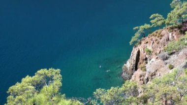 Türkiye 'de deniz kıyısındaki dağ kıyısında insanlar masmavi şeffaf denizde yüzüyor.