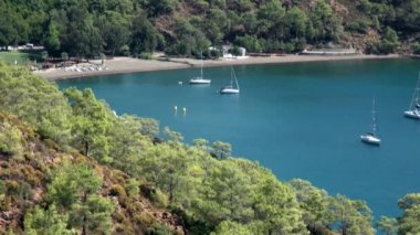 Beyaz yatlar arka planda yelken açıyor ve kıyı şeridinde dağlar..