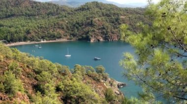 Beyaz yatlar arka planda yelken açıyor ve kıyı şeridinde dağlar..