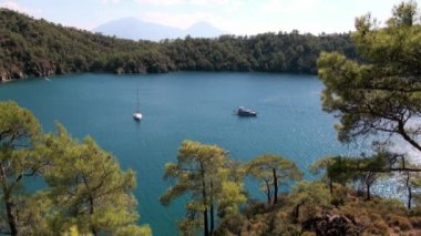 Beyaz yatlar arka planda yelken açıyor ve kıyı şeridinde dağlar..