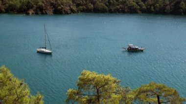 Beyaz yatlar arka planda yelken açıyor ve kıyı şeridinde dağlar..