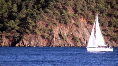 Beyaz yatlar gün ışığında yelken açar. Deniz ve dağların arka planında..