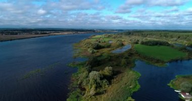 Arka planda gökyüzü ve çarpıcı manzara manzaralı bulutlarla çevrili bir nehir üzerinde evleri ve bahçeleri olan kırsal arazi aracı video panoraması. Açık hava iklimi kavramı.