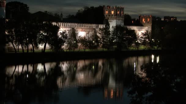 People walk near Novodevichy monastery on shore of pond at night. — Stock Video