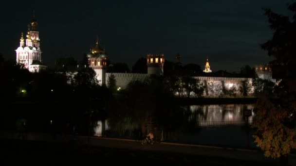La gente camina cerca del convento Novodevichy en la orilla del estanque por la noche. — Vídeos de Stock