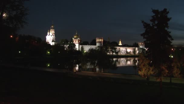 La gente camina cerca del convento Novodevichy en la orilla del estanque por la noche. — Vídeo de stock