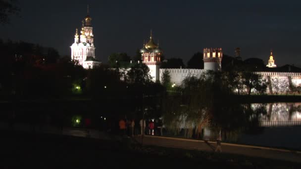 La gente camina cerca del convento Novodevichy en la orilla del estanque por la noche. — Vídeo de stock