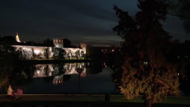 La gente camina cerca del convento Novodevichy en la orilla del estanque por la noche. — Vídeo de stock