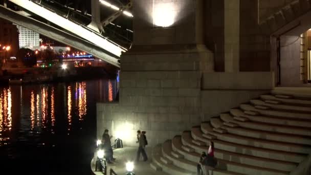 Menschen laufen nachts in Moskau auf gläserner Brückenkonstruktion über Fluss. — Stockvideo