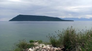 Kayalık Baykal Gölü kıyılarının arka planında yeşil ağaçlar olan ada..
