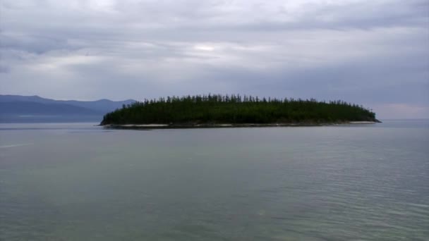 Sziget zöld fákkal a Bajkál-tó sziklás partvidékének hátterében. — Stock videók