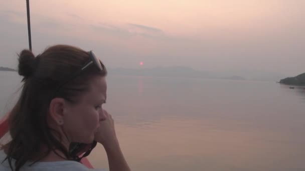 Frau in weißem T-Shirt mit Kamera sitzt in Boot mit rotem Bug im Meer. — Stockvideo