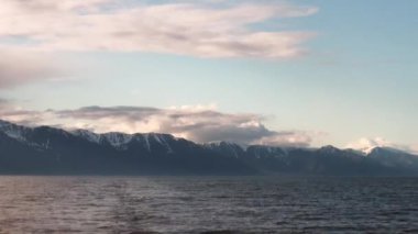 Karanlık gökyüzünün arka planında su yüzeyinde dalgalar ve gün batımında gri bulutlar.