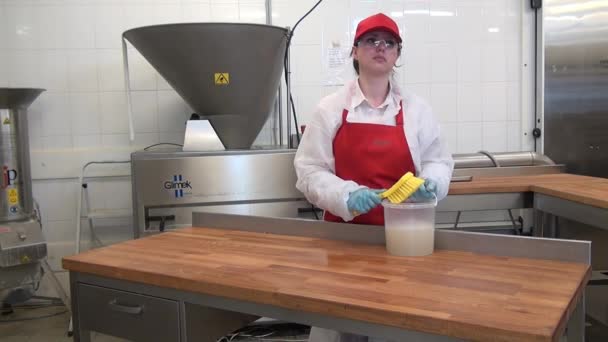 Vrouwelijke werkster in rood schort en pet desinfecteert houten tafel in industriële werkplaats. — Stockvideo