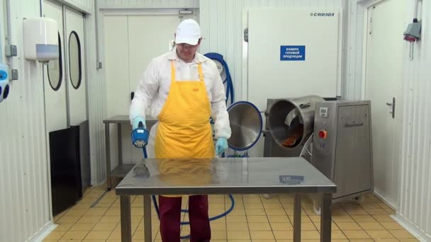 Człowiek pracownik w białym płaszczu i żółty fartuch myje stół w warsztacie przemysłowym. — Wideo stockowe