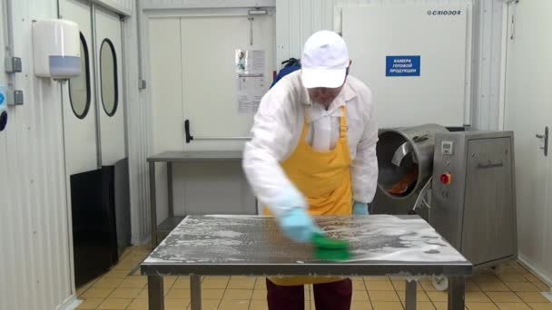 Man arbeider in witte jas en gele schort wast tafel in industriële werkplaats. — Stockvideo