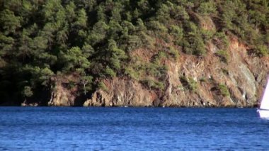 Beyaz yatlar gün ışığında yelken açar. Deniz ve dağların arka planında..