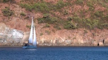 Beyaz yatlar gün ışığında yelken açar. Deniz ve dağların arka planında..