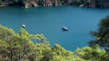 Beyaz yatlar arka planda yelken açıyor ve kıyı şeridinde dağlar..